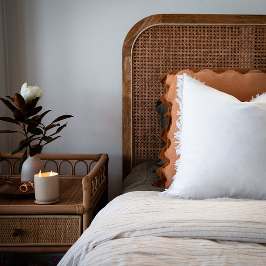 Thoughtfully styled bedroom with luxe European Flax Linen cushions and sheets, with a hand poured soy candle on the rattan bedside table