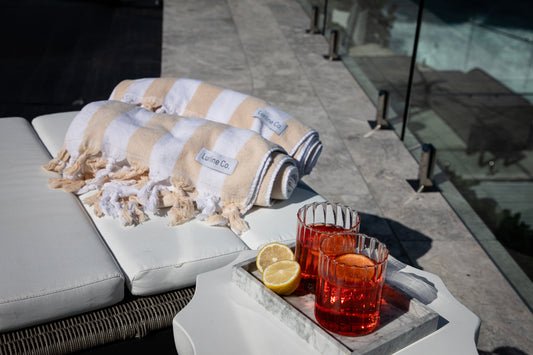 Lurline Co. Barefoot Striped Plush Oversized Beach Towels rolled up next to cocktails in the Lurline Co. Ripple Tumblers styled on a balcony overlooking the Sydney Beaches